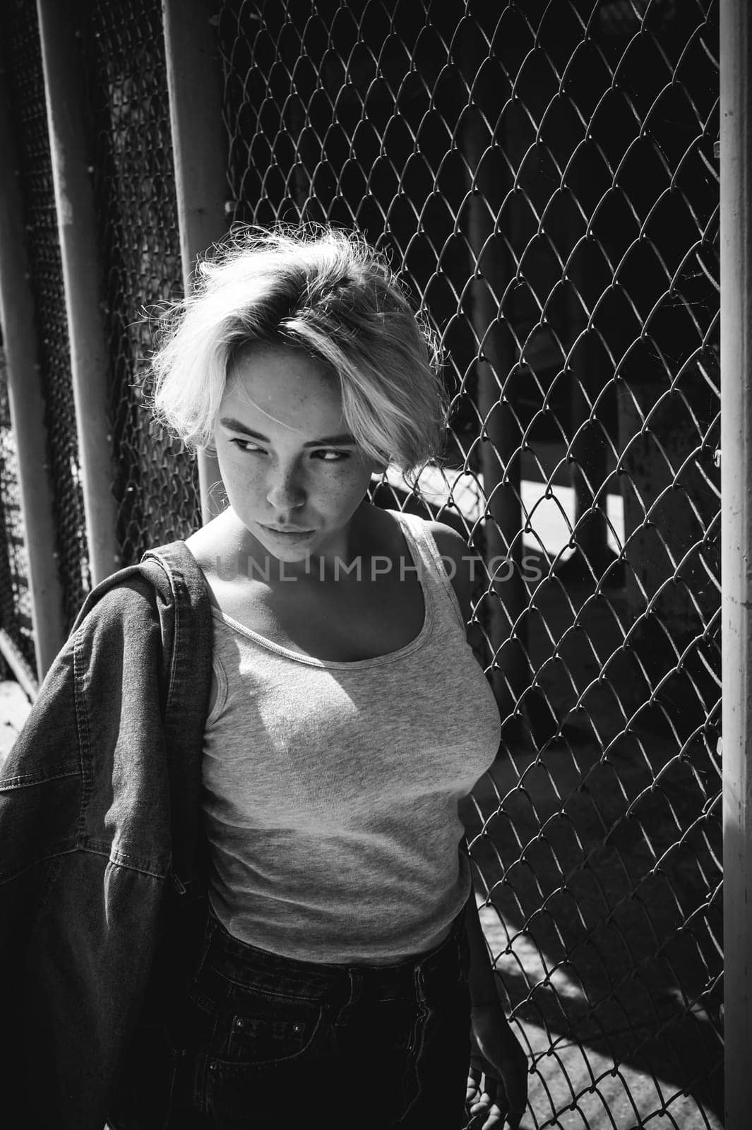 young woman in jeans clothes outdoors. portrait of a girl with freckles on her face, stylish girl on a fence of a grid, a sunny summer day...