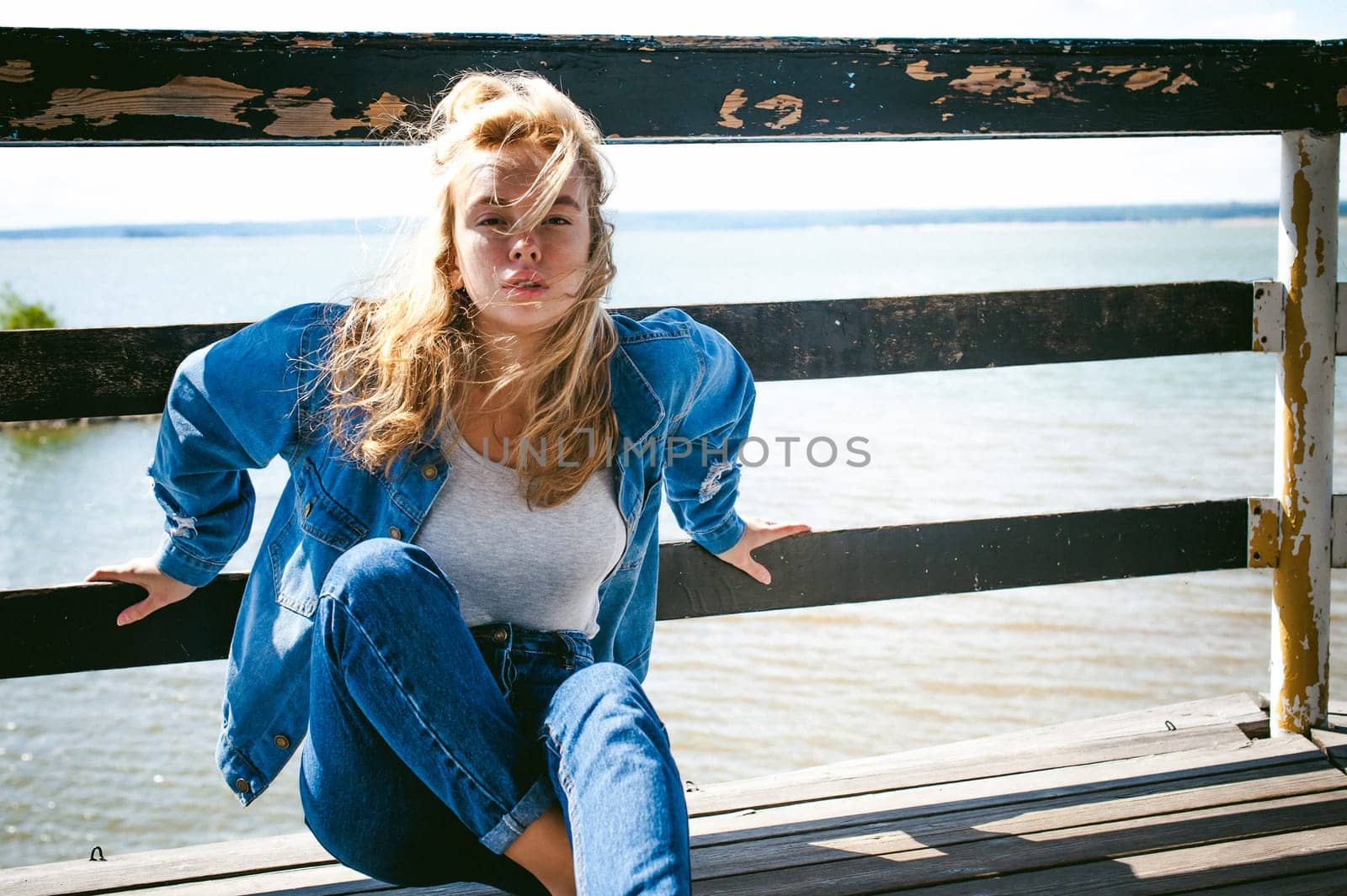 young beautiful woman in jeans clothes outdoors. portrait of a girl with freckles on her face, stylish girl on sea beach rescue tower, on a sunny summer autumn day.
