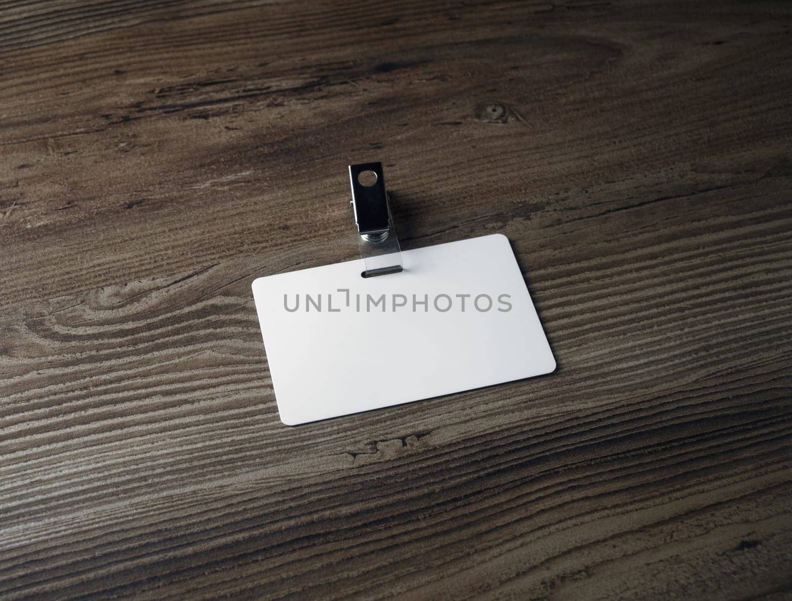 Blank badge mockup on wooden background. White plastic id card. Space for text.