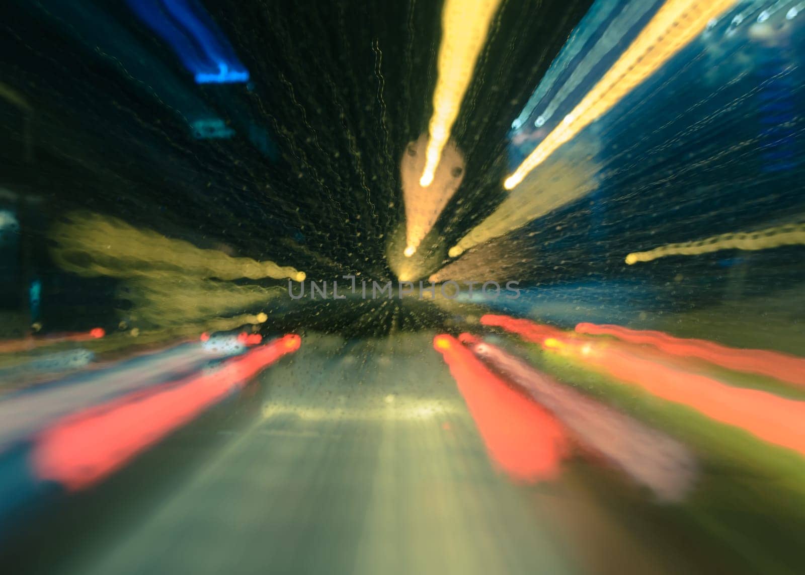 Blurred night raindrops on windscreen bokeh and traffic lights trail background. Motion zoom blur with retro filtered effect.