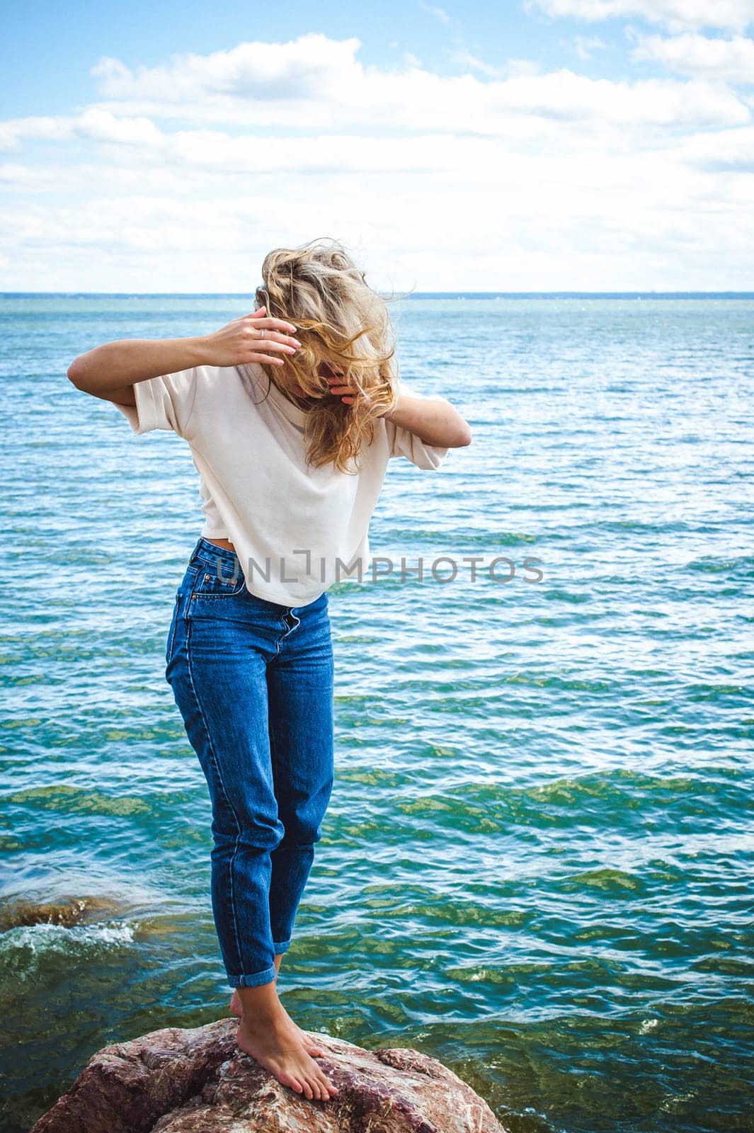 Portrait young woman on stones near sea. Beautiful girl is resting on coast, enjoying outdoor recreation.