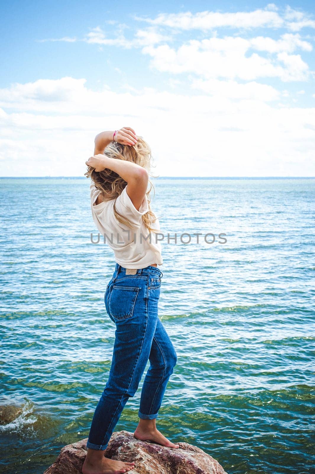Portrait young woman on stones near sea. Beautiful girl is resting on coast, enjoying outdoor recreation.
