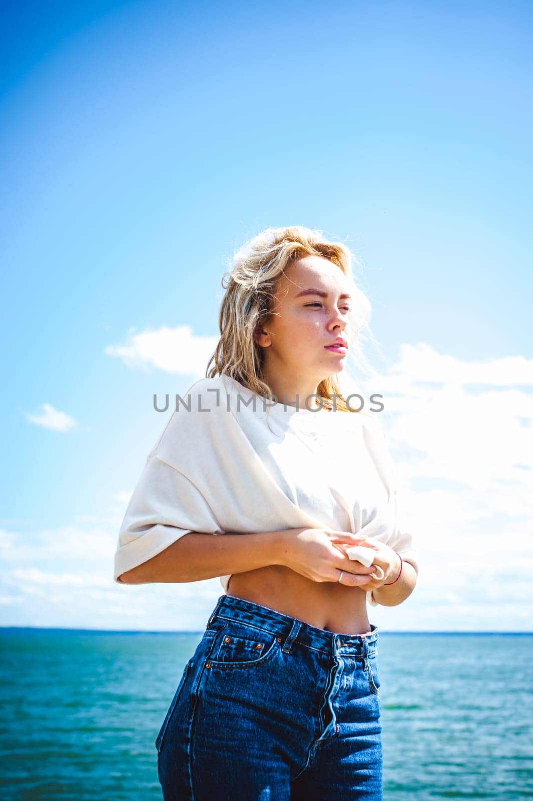 Portrait young woman on stones near sea. Beautiful girl is resting on coast, enjoying outdoor recreation.