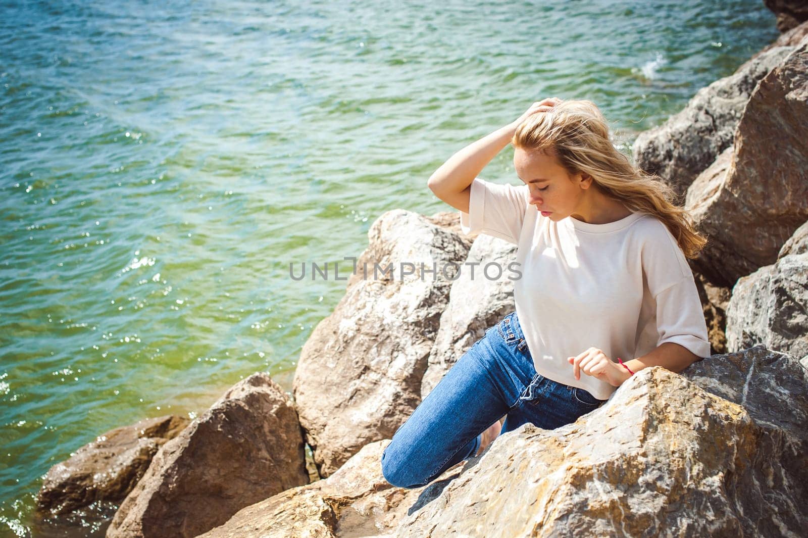 Portrait young woman on stones near sea. Beautiful girl is resting on coast, enjoying outdoor recreation.