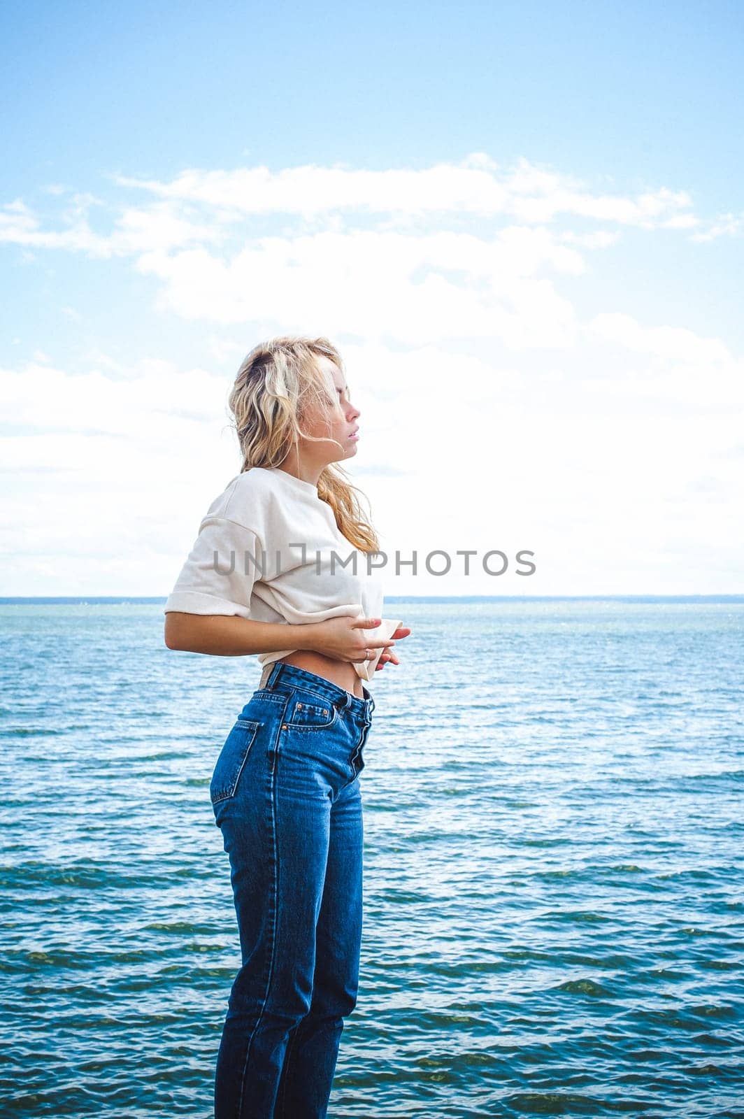 Portrait young woman on stones near sea. Beautiful girl is resting on coast, enjoying outdoor recreation.