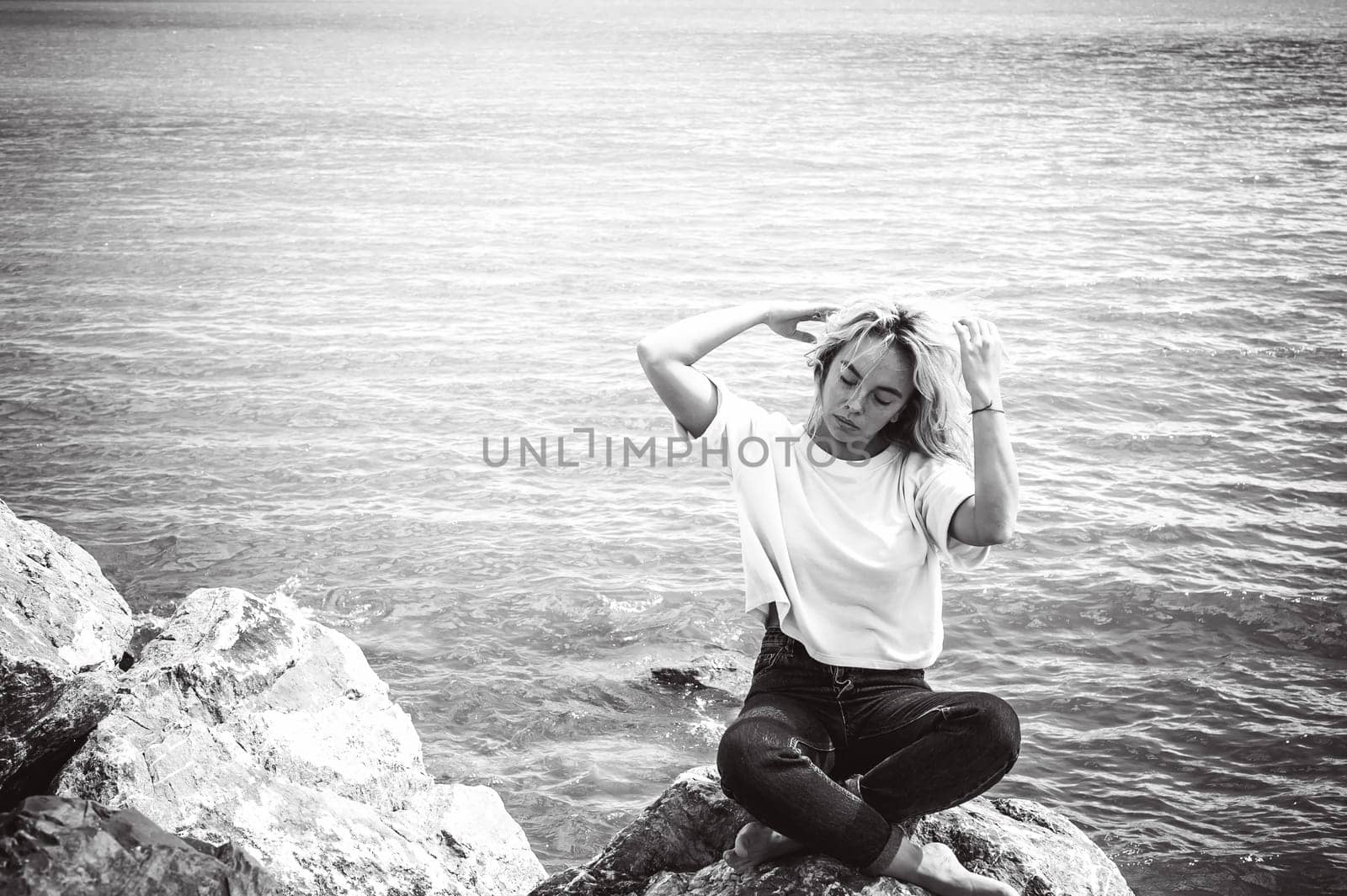 Portrait young woman on stones near sea. Beautiful girl is resting on coast, enjoying outdoor recreation.