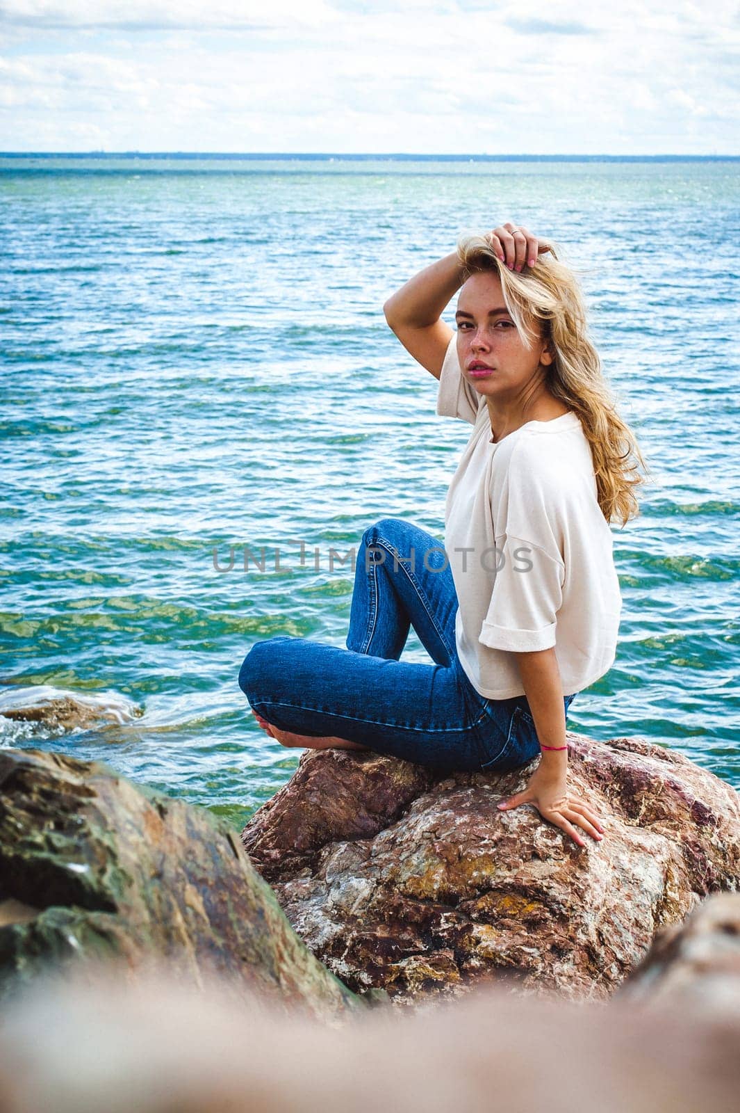 Portrait young woman on stones near sea. Beautiful girl is resting on coast, enjoying outdoor recreation.