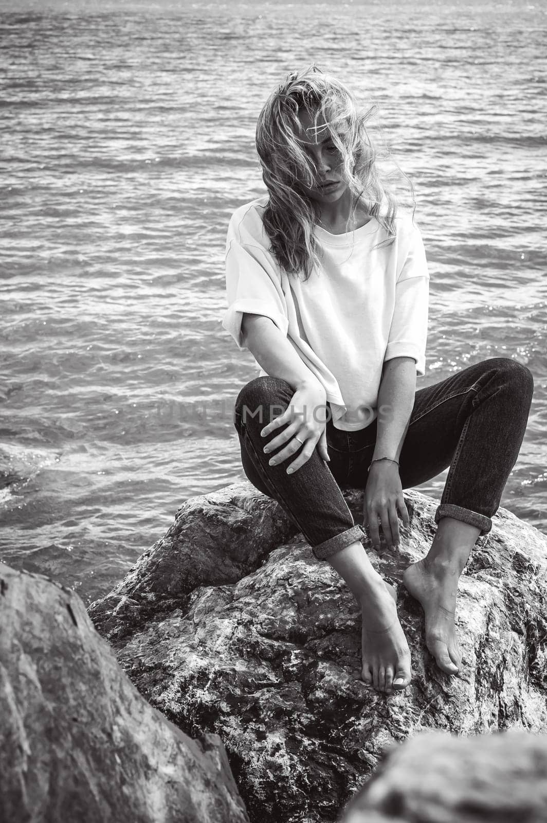 Portrait young woman on stones near sea. Beautiful girl is resting on coast, enjoying outdoor recreation.