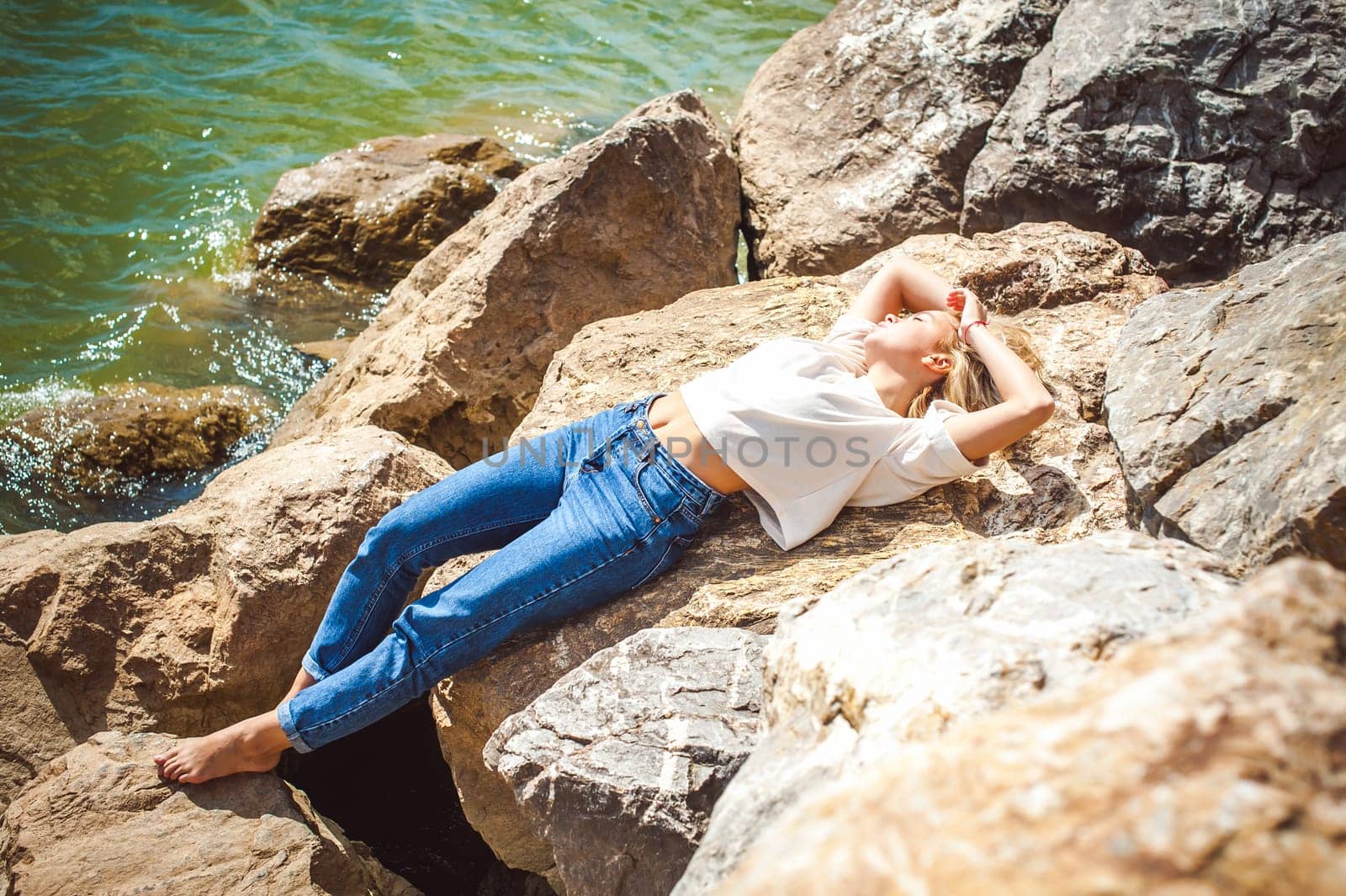 Portrait young woman on stones near sea. Beautiful girl is resting on coast, enjoying outdoor recreation.