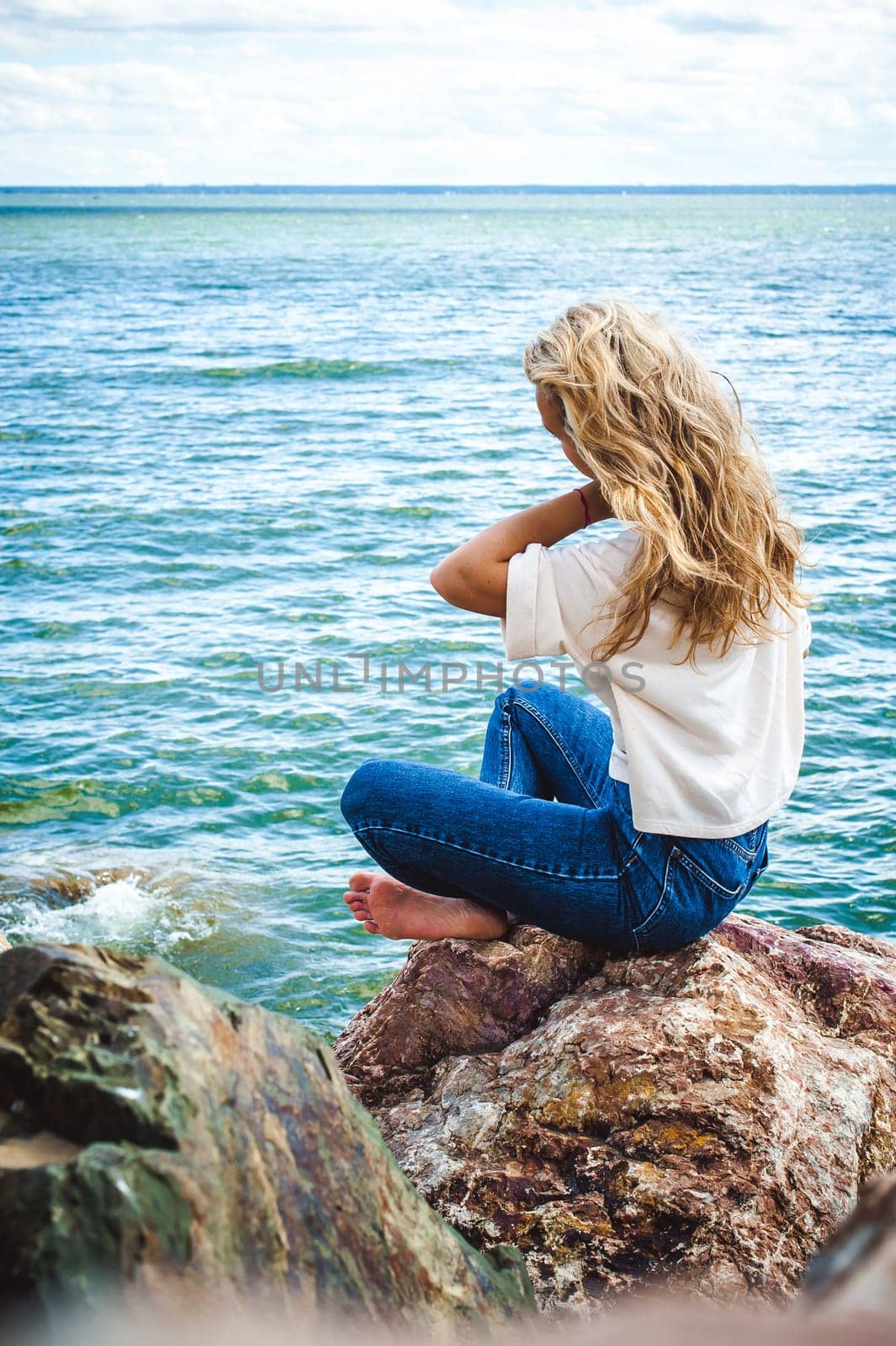 Portrait young woman on stones near sea. Beautiful girl is resting on coast, enjoying outdoor recreation.