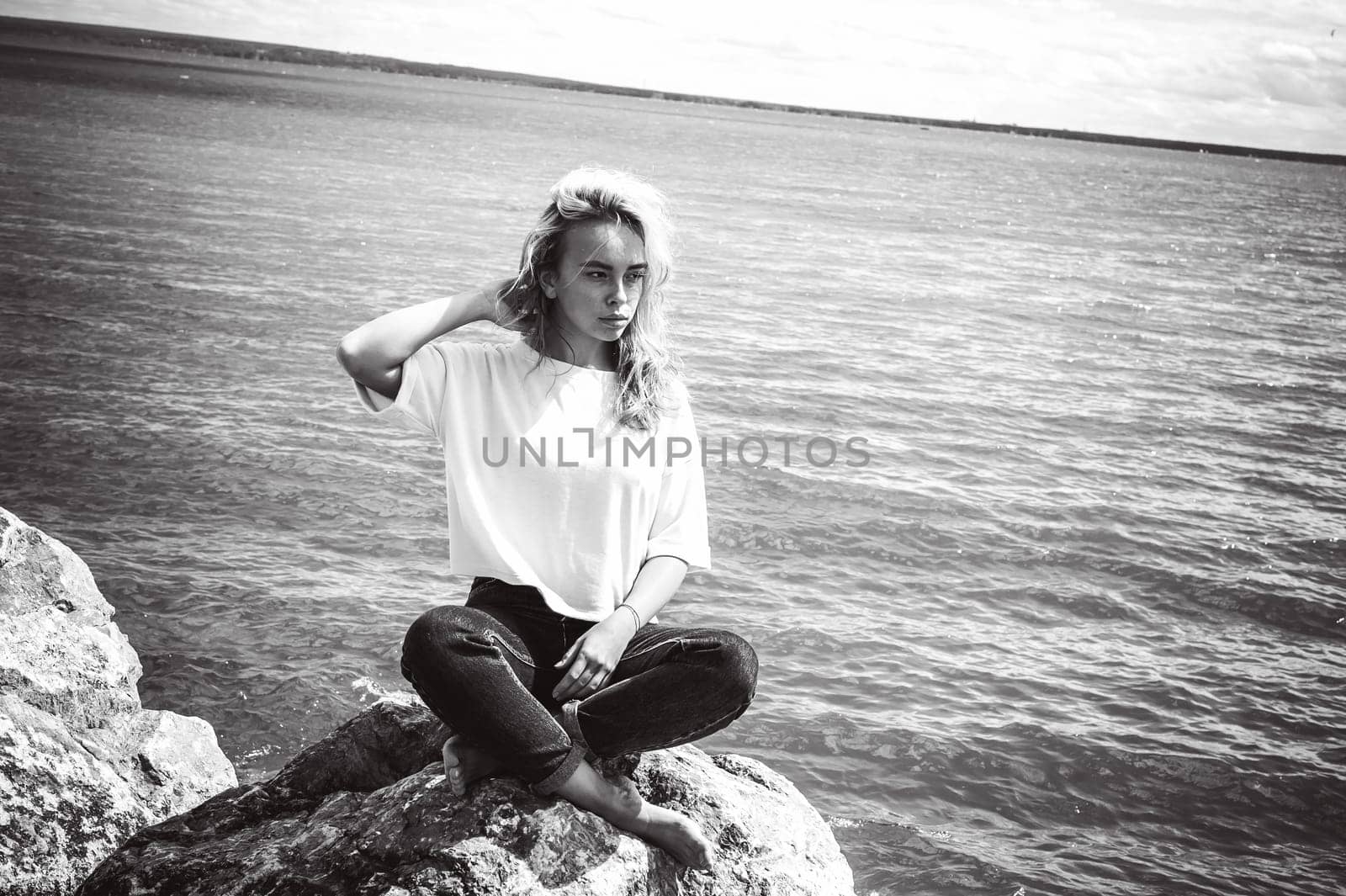 Portrait young woman on stones near sea. Beautiful girl is resting on coast, enjoying outdoor recreation.