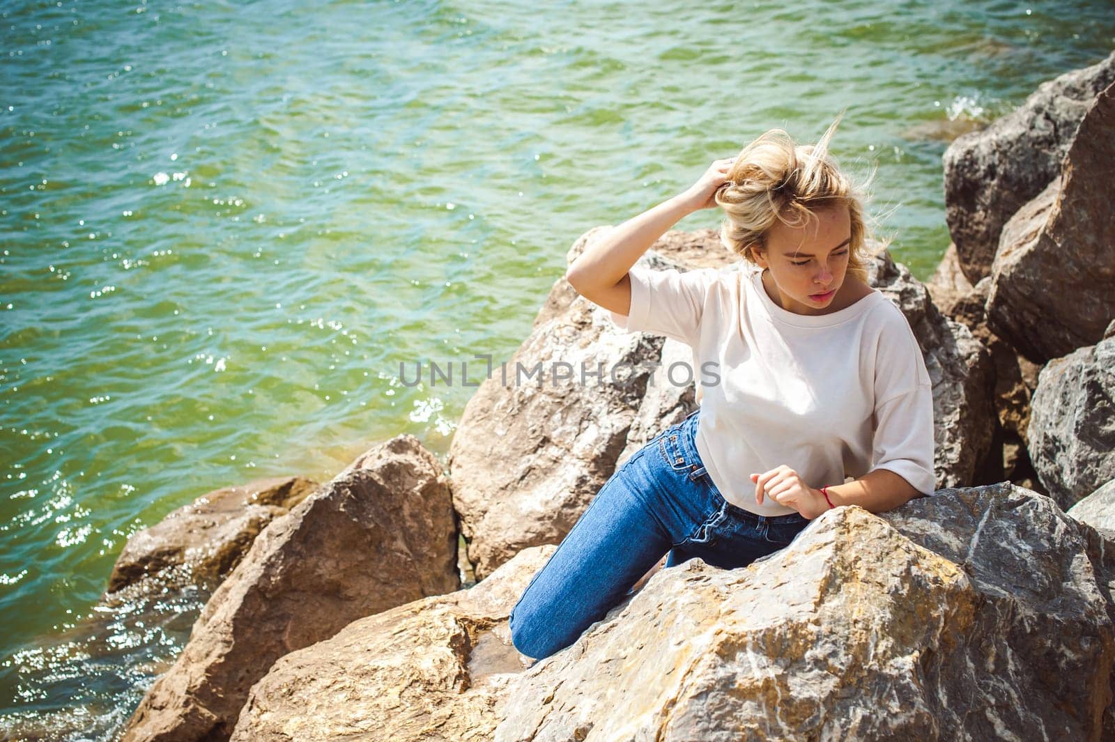 Portrait young woman on stones near sea. Beautiful girl is resting on coast, enjoying outdoor recreation.