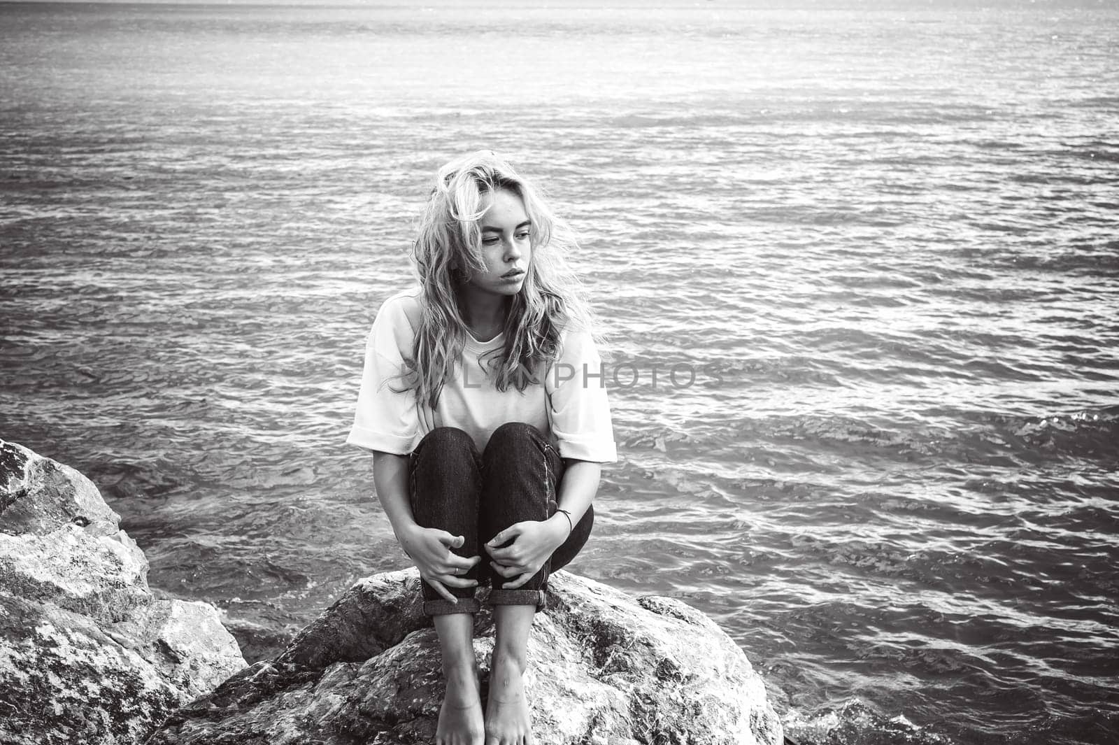 Portrait young woman on stones near sea. Beautiful girl is resting on coast, enjoying outdoor recreation.