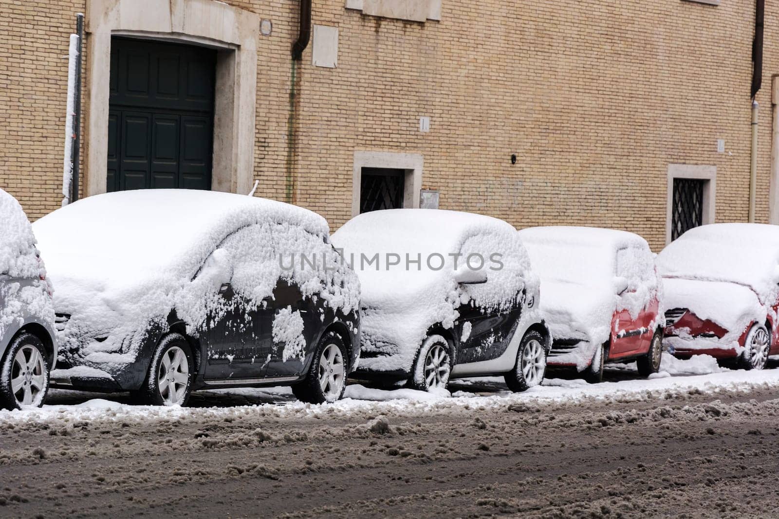 cars parked in a row covered by snow with already melted snow on the road