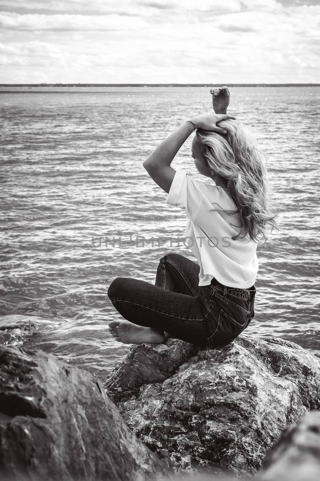 Portrait young woman on stones near sea. Beautiful girl is resting on coast, enjoying outdoor recreation.