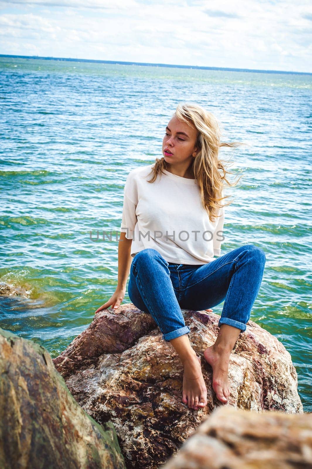 Portrait young woman on stones near sea. Beautiful girl is resting on coast, enjoying outdoor recreation.