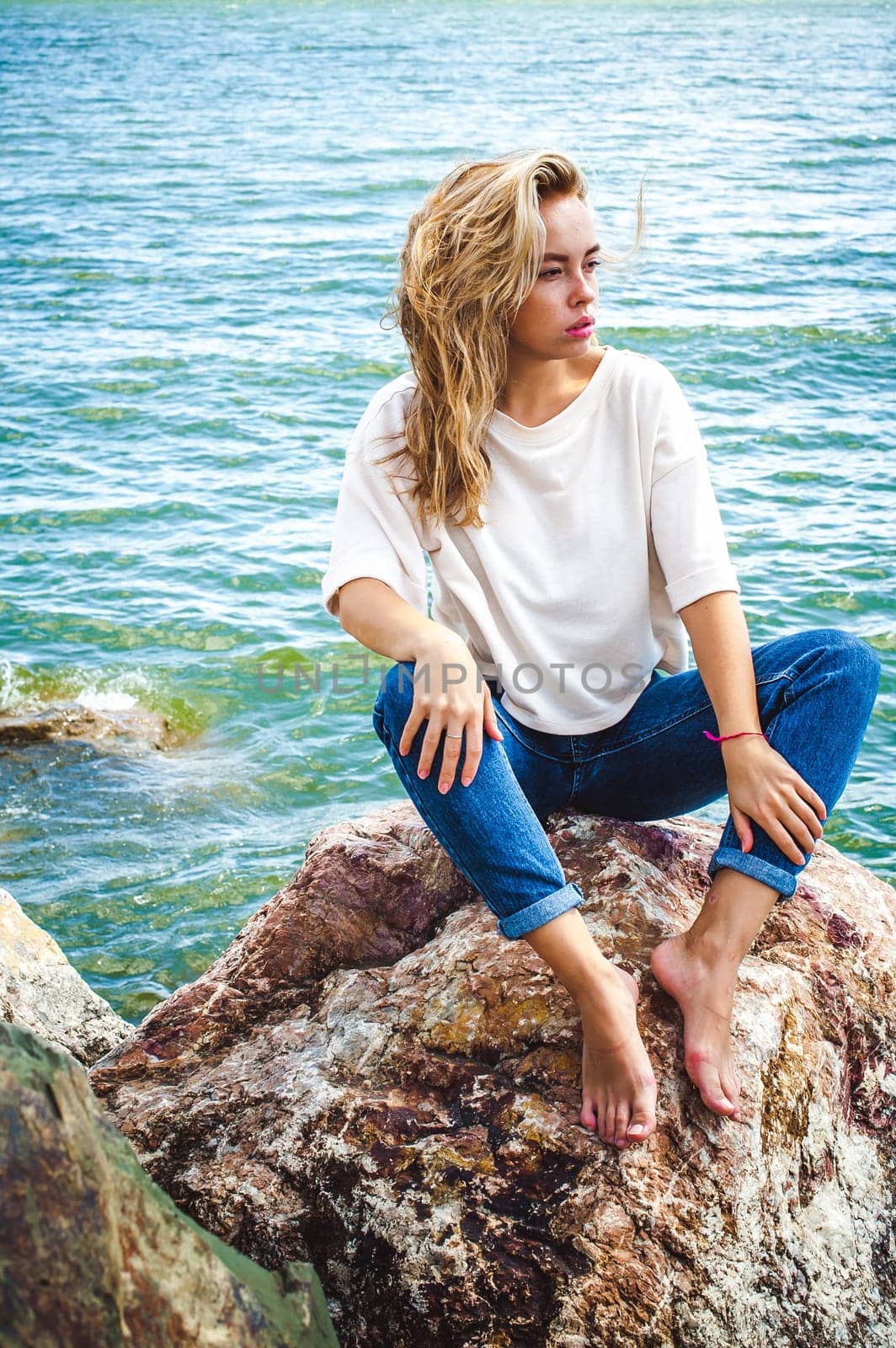 Portrait young woman on stones near sea. Beautiful girl is resting on coast, enjoying outdoor recreation.