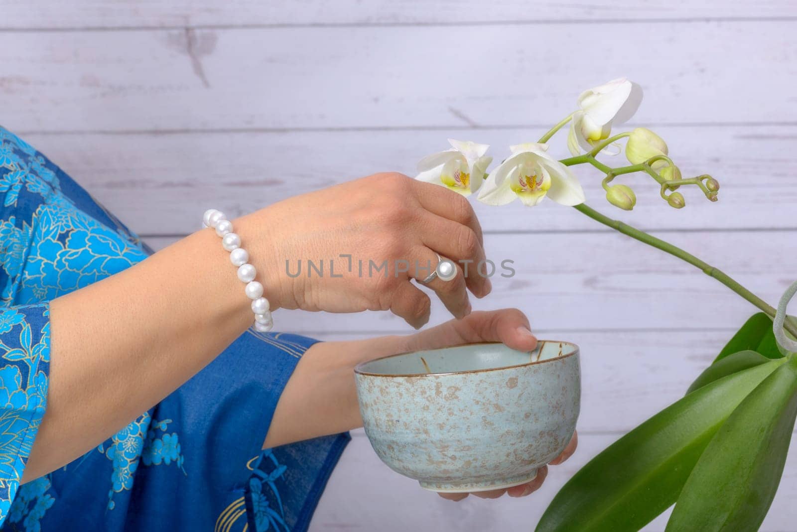Woman cares for white orchid, wearing ring of Japanese white pearls.