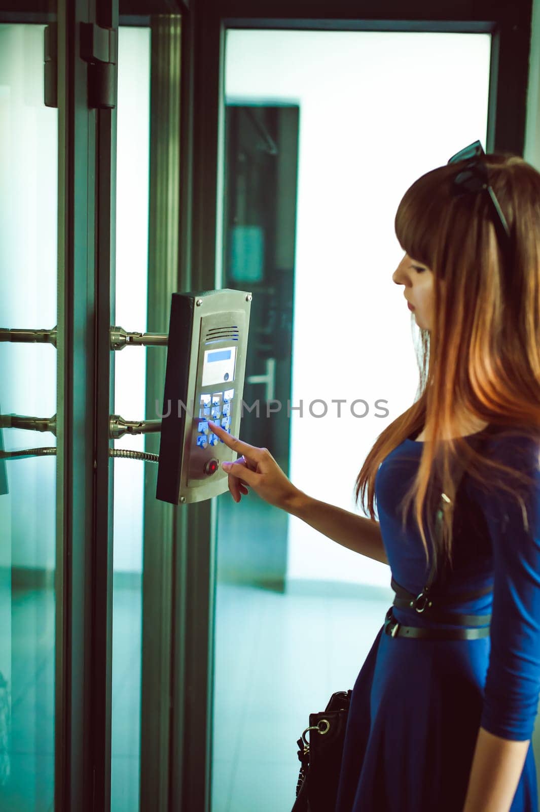 attractive woman in a blue elegant dress, dials code into intercom, at entrance of house