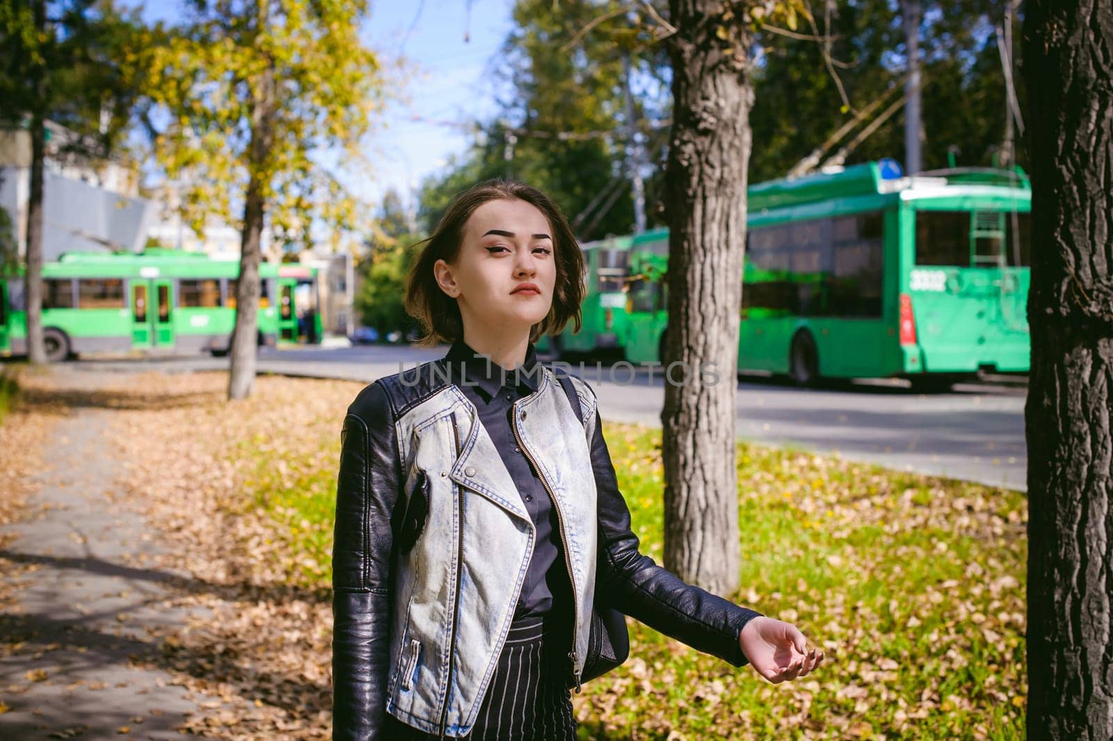 street portrait of a girl student, fashionably dressed in dark clothes, with a black backpack and denim jacket autumn sunny day