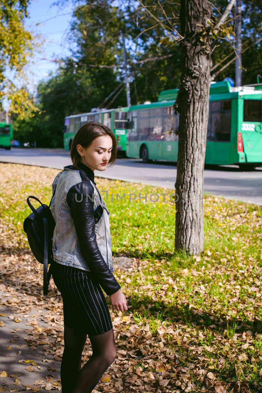 street portrait of a girl student, fashionably dressed in dark clothes, with a black backpack and denim jacket autumn sunny day