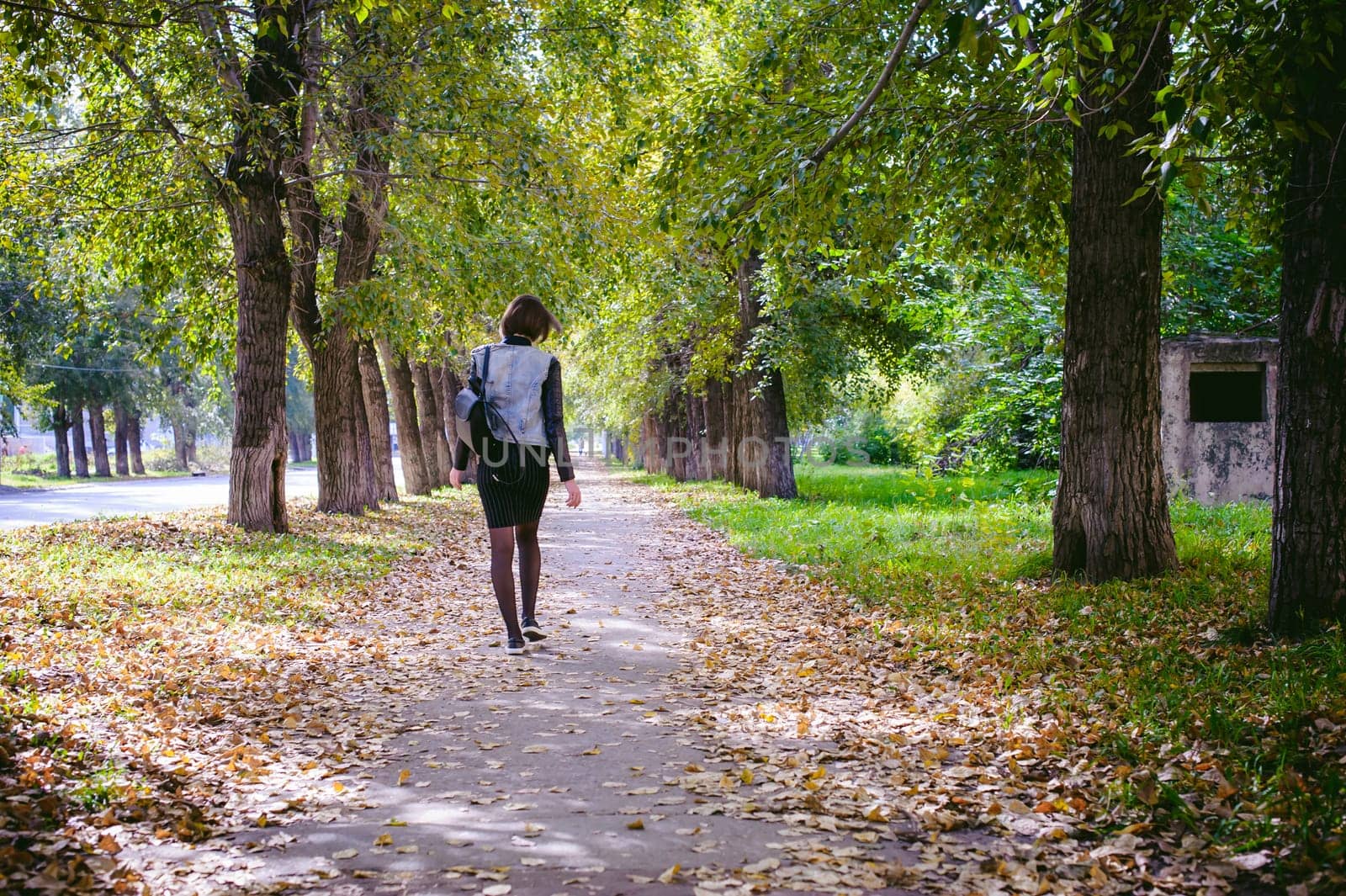 street portrait of a girl student, fashionably dressed in dark clothes, with a black backpack and denim jacket autumn sunny day