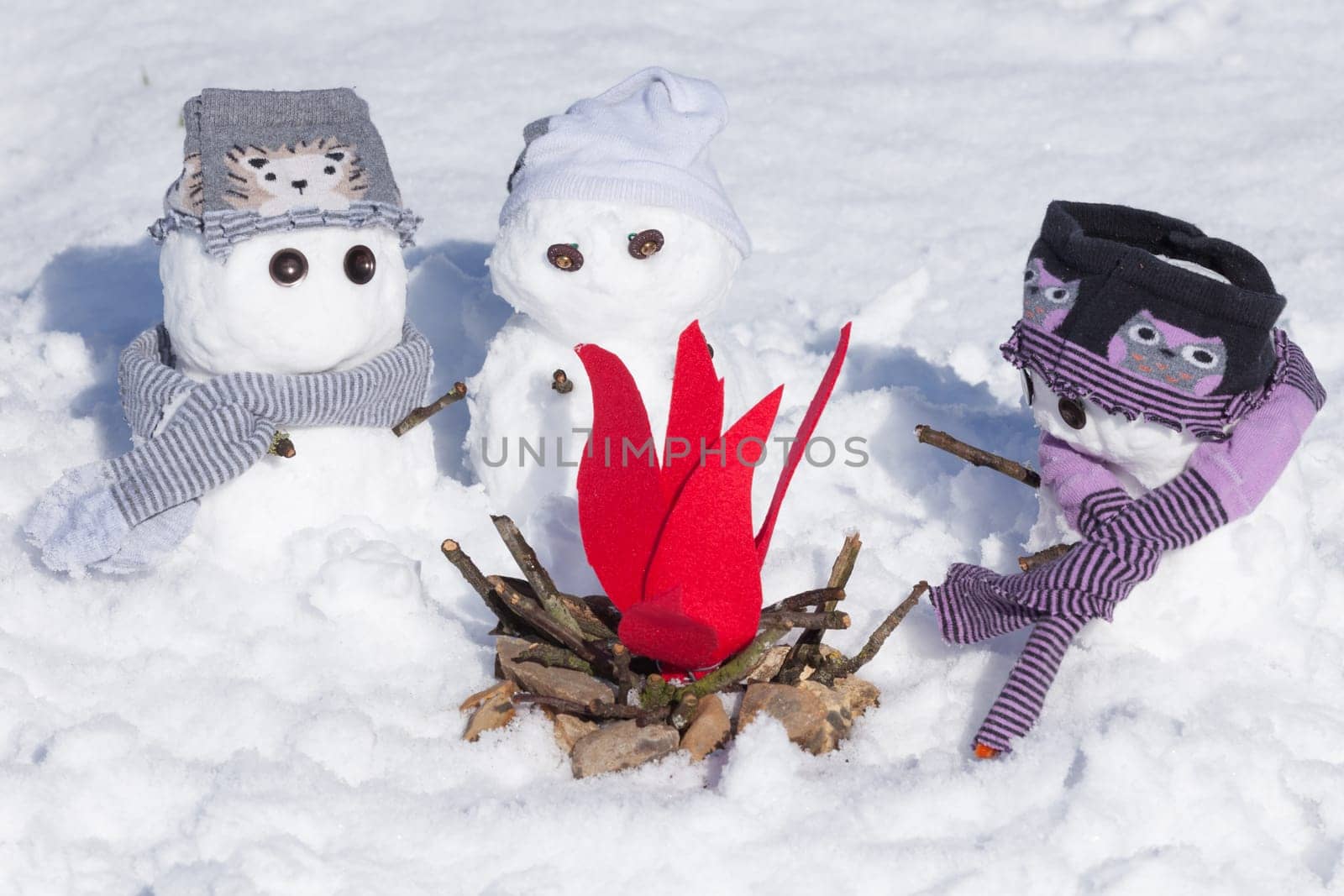 Cute little snowmen dressed for winter, huddled around a fire trying to keep warm. Snow covered scene in Norfolk UK