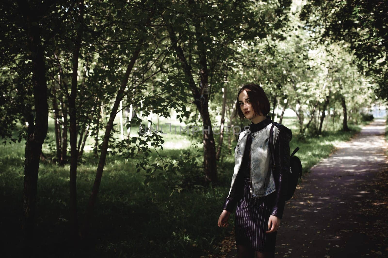 street portrait of a girl student, fashionably dressed in dark clothes, with a black backpack and denim jacket autumn sunny day