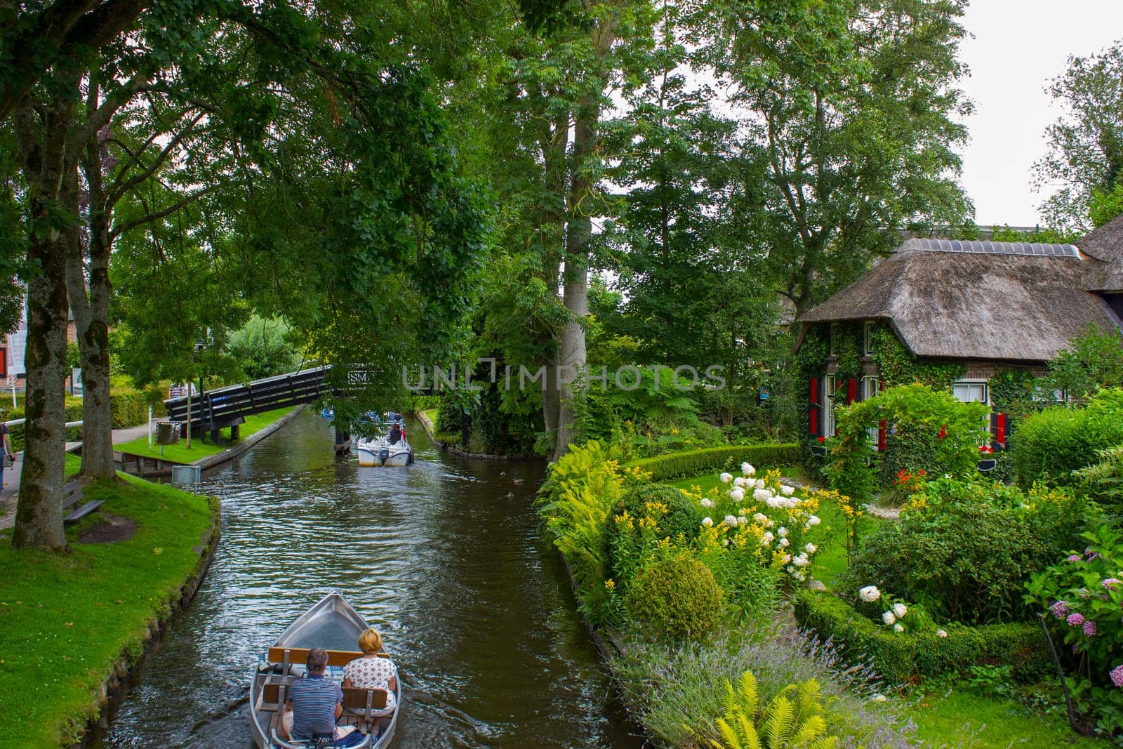 GIETHOORN, NETHERLANDS - AUGUST 01 2017: Unknown visitors in the sightseeing boating trip in a canal in Giethoorn. The beautiful houses and gardening city is know as "Venice of the North""."
