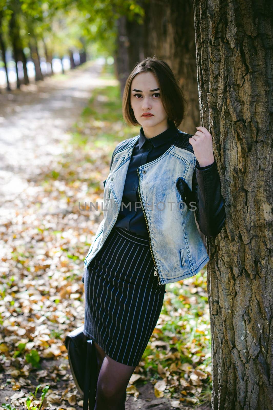 street portrait of a girl student, fashionably dressed in dark clothes, with a black backpack and denim jacket autumn sunny day