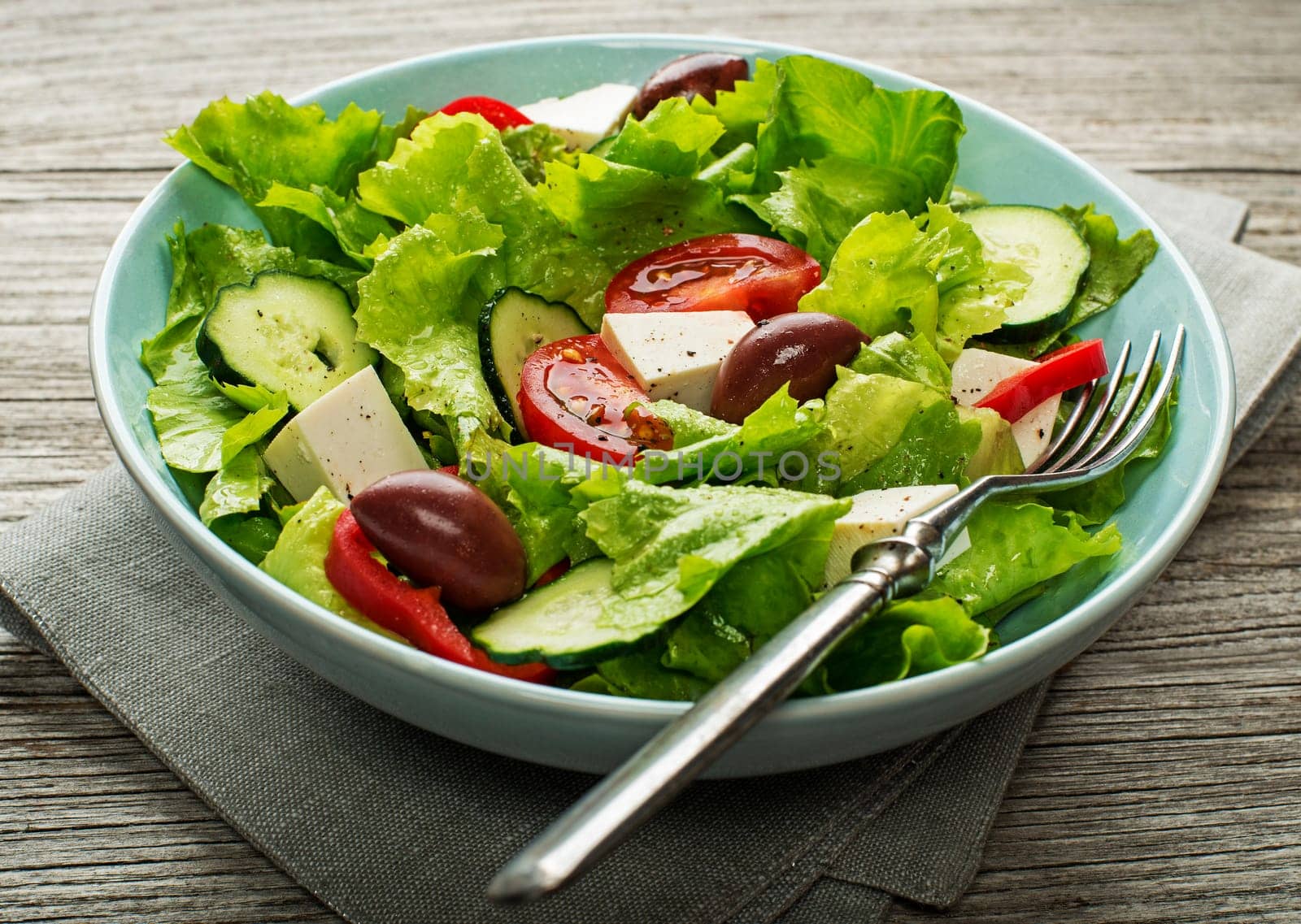 Green lettuce Salad with feta cheese and fresh vegetables on wooden background.