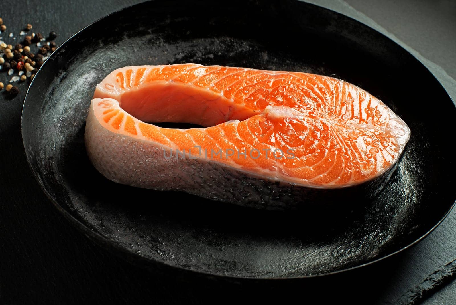 Slice of red salmon fish with spices on black background.