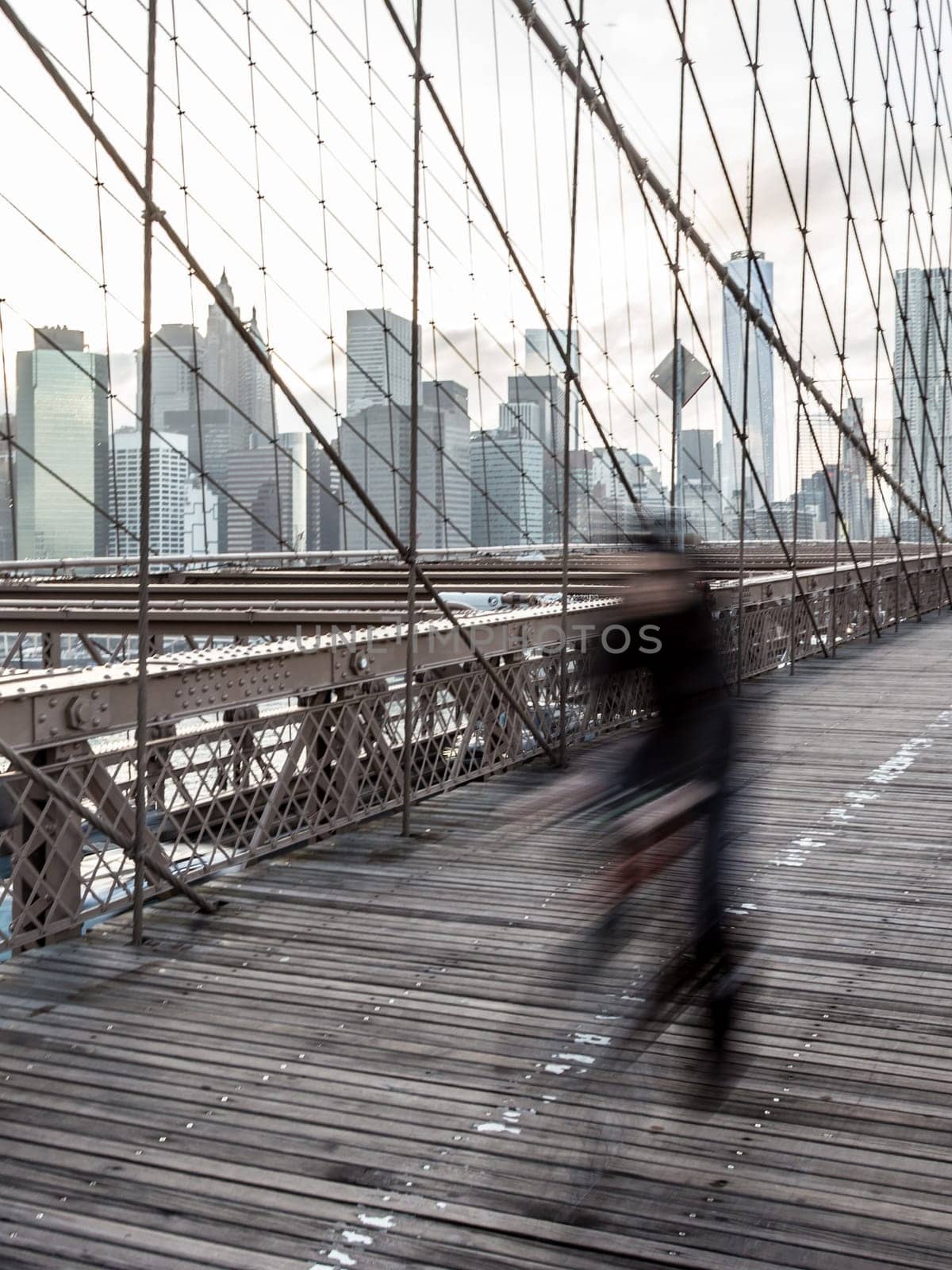 Blured cyclist cycling across Brooklyn bridge. New York City Manhattan downtown skyline in sunset with skyscrapers illuminated over East River panorama as seen from Brooklyn bridge.
