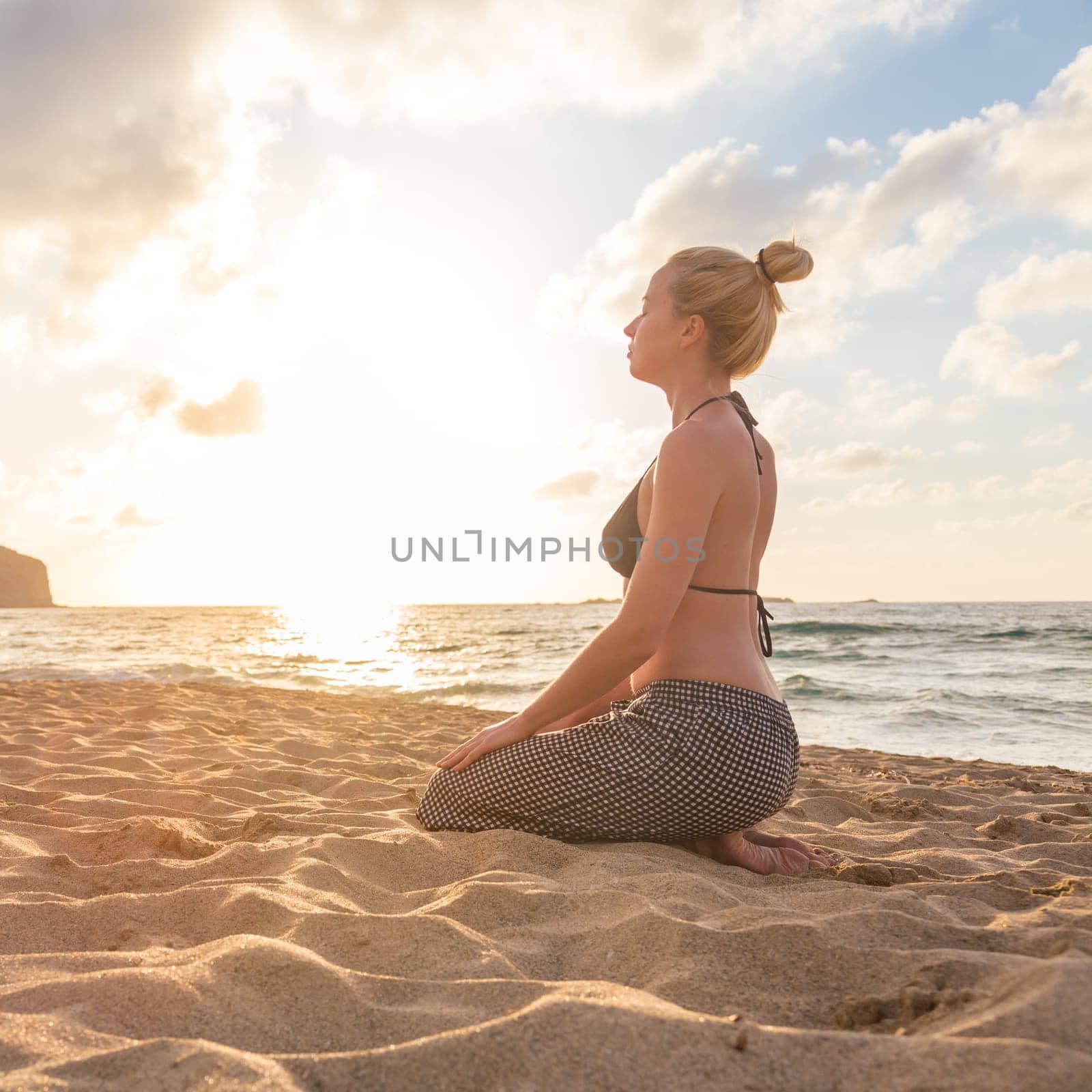 Active young woman streching and practicing yoga on beach at sunset.
