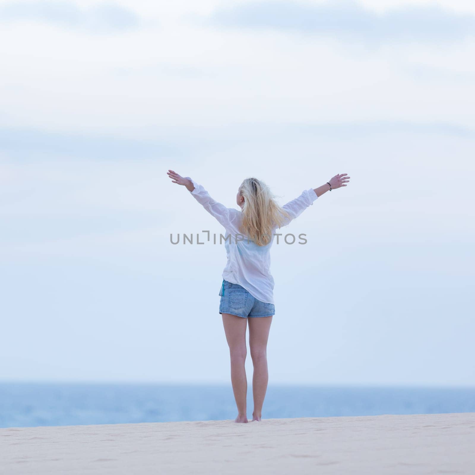 Relaxed woman enjoying freedom feeling happy at beach at dusk. Serene relaxing woman in pure happiness and elated enjoyment with arms raised outstretched up.