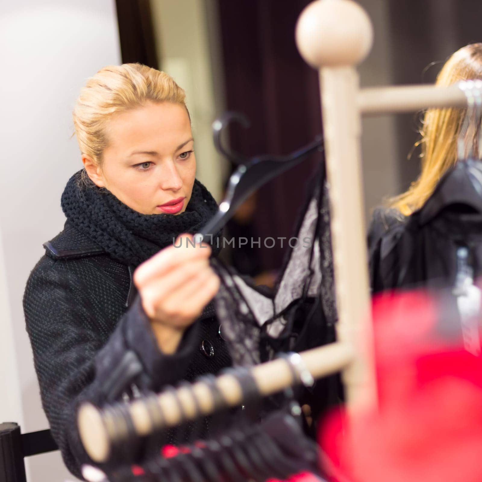 Woman shopping clothes. Shopper looking at clothing indoors in store. Beautiful blonde caucasian female model wearing casual winter clothing and black scarf.