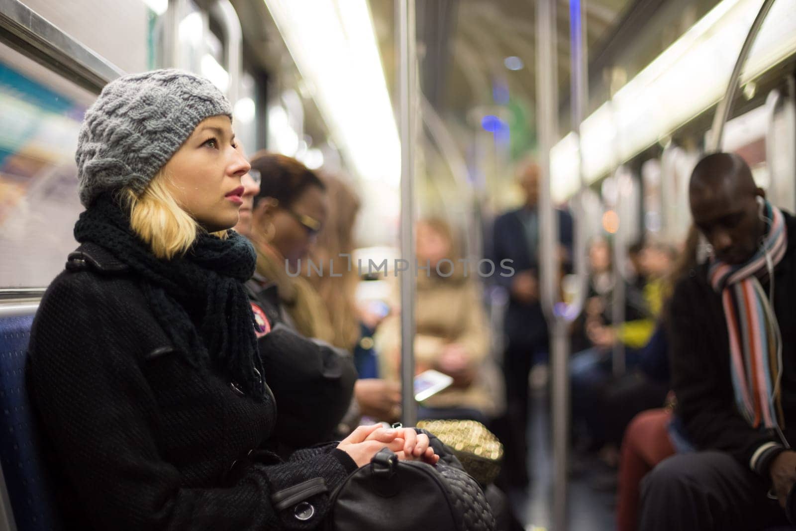 Beautiful blonde caucasian lady wearing winter coat traveling by metro in rush hour. Public transport.
