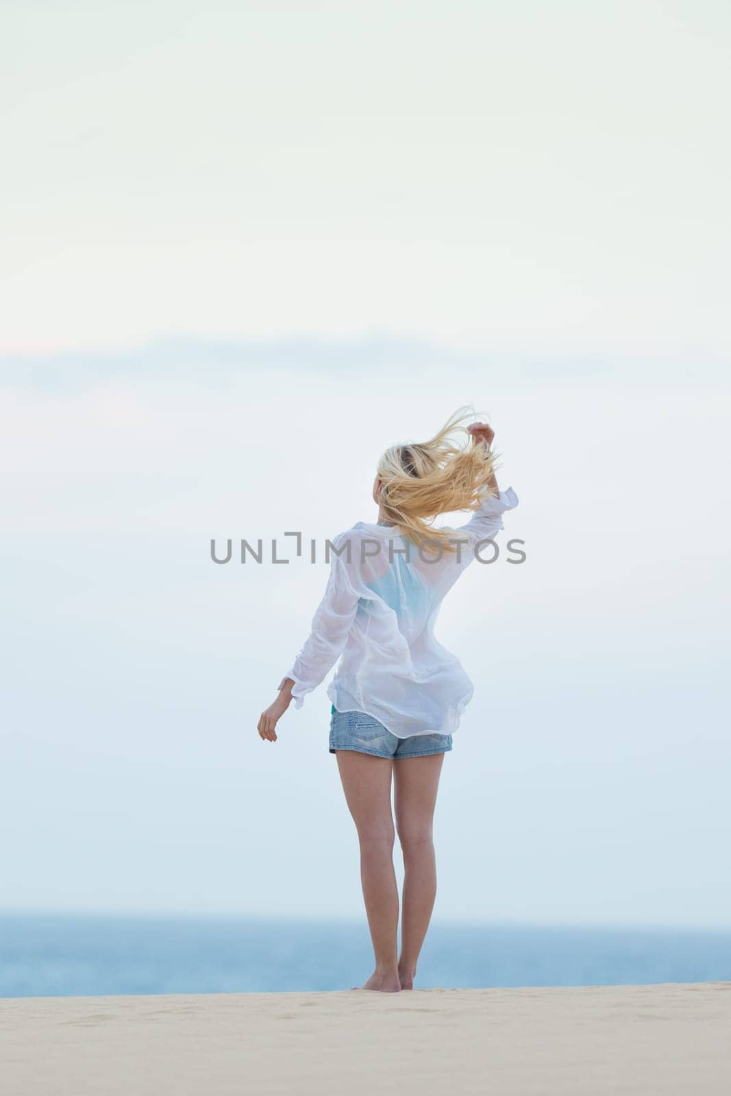 Meditative, sensual blonde woman wearing white loose casual shirt on vacations, looking at horizon, enjoying peaceful early morning.