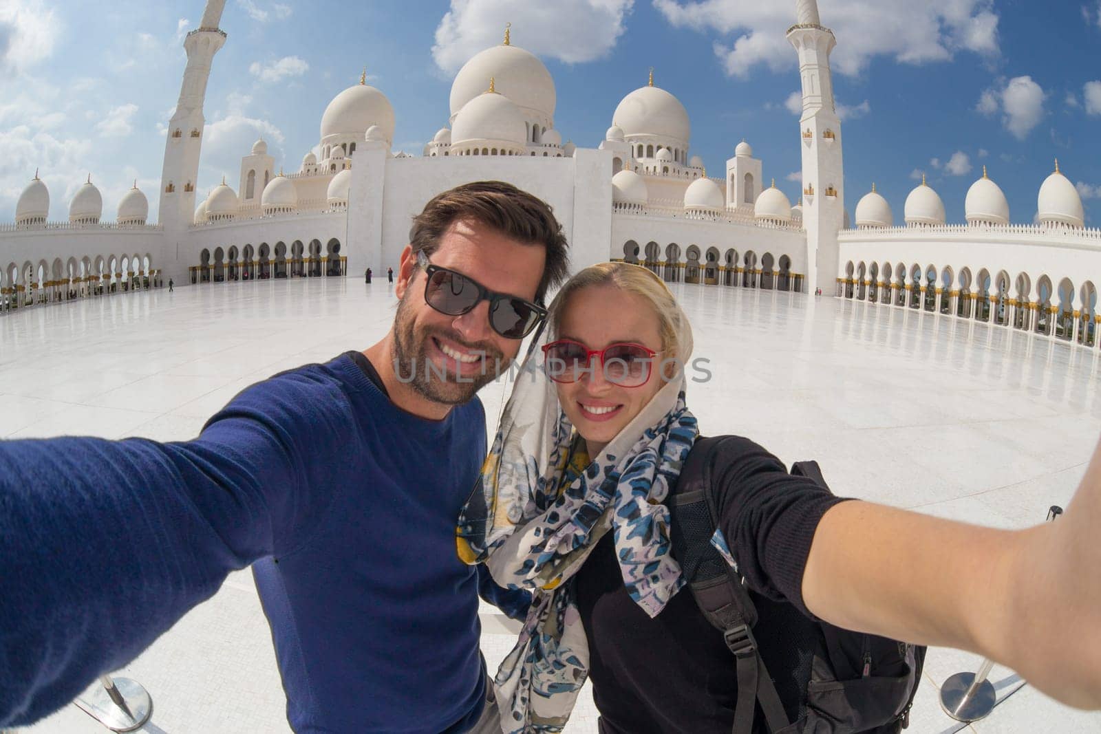Tourist couple taking selfie in the courtyard of famous Sheikh Zayed Grand Mosque in Abu Dhabi, United Arab Emirates.