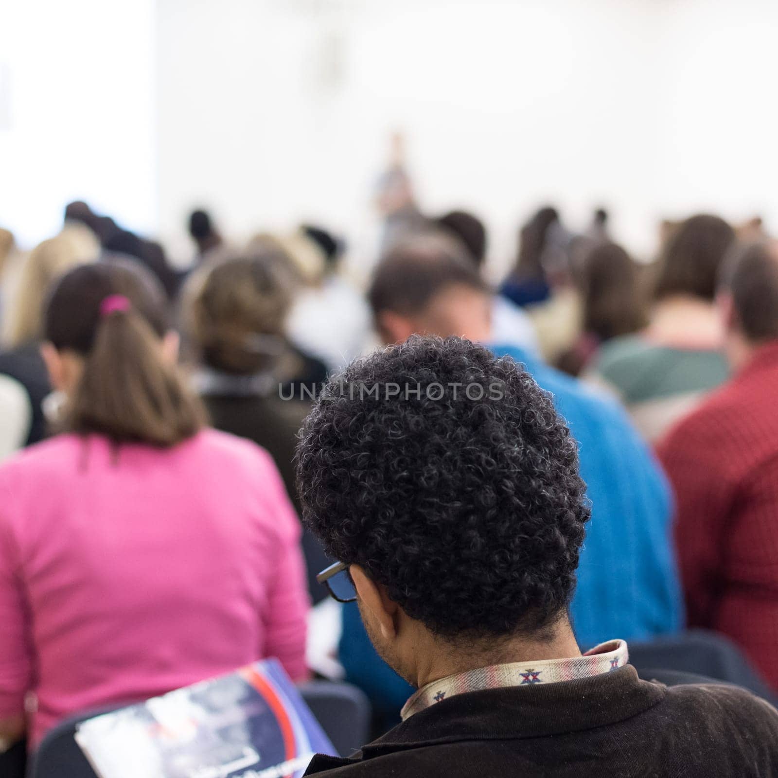 Business and entrepreneurship symposium. Female speaker giving a talk at business meeting. Audience in conference hall. Rear view of unrecognized participant in audience. Copy space on whitescreen.