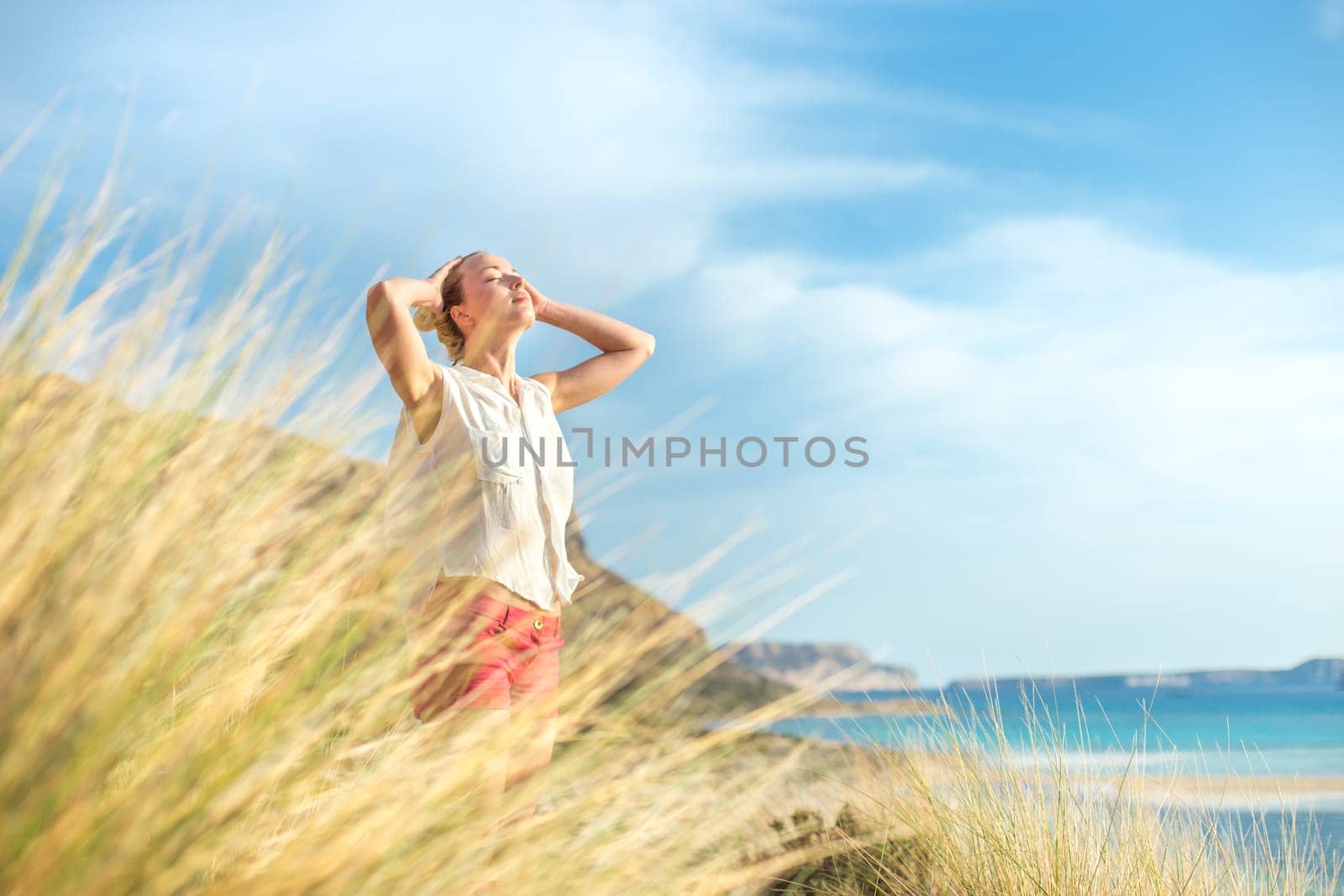 Relaxed woman, arms rised, enjoying sun, freedom and life an a beautiful beach. Young lady feeling free, relaxed and happy. Concept of vacations, freedom, happiness, enjoyment and well being.