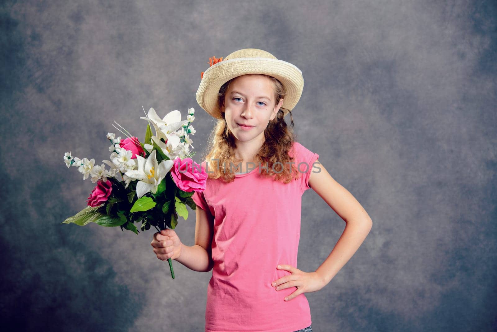 nice blond girl with straw hat and bouquet of flowers in front of gray background