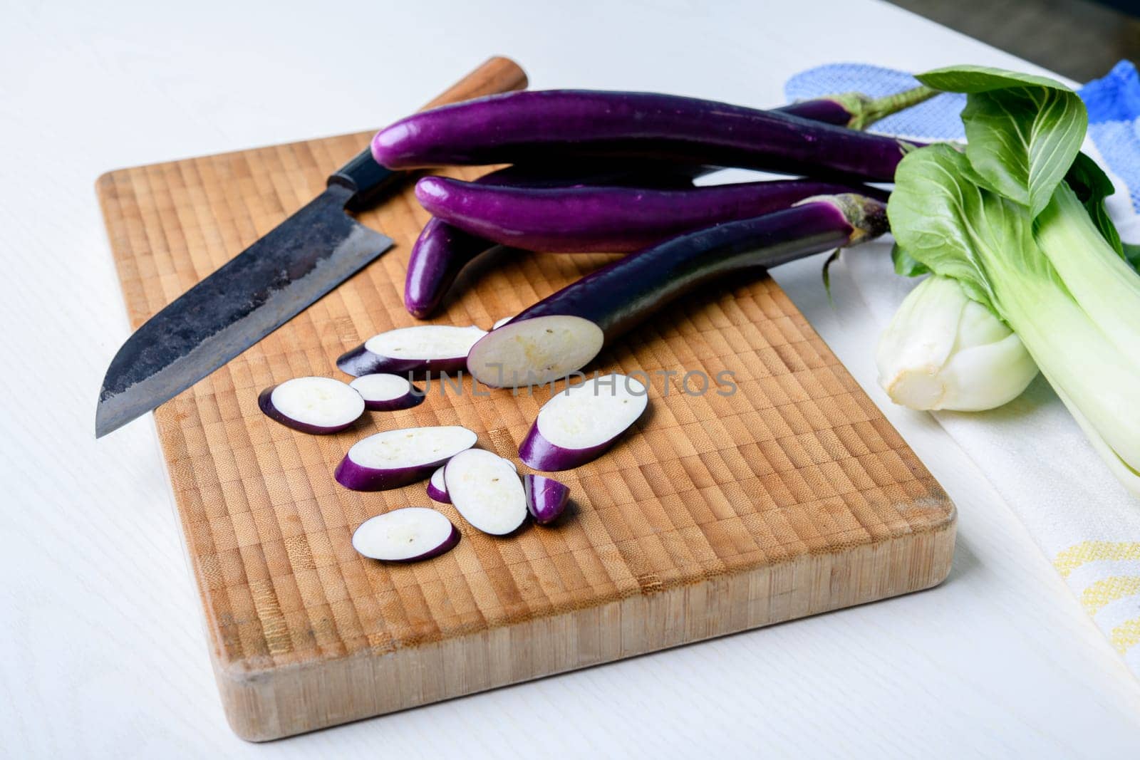 japanese eggplant on wooden board with cooking knife and pak choi salad