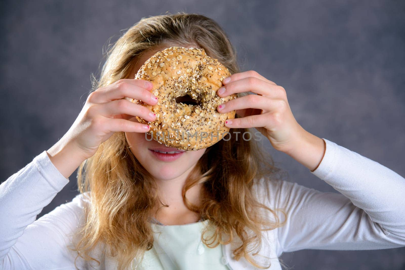 nice blond girl in front of gray background looking through a big bagel
