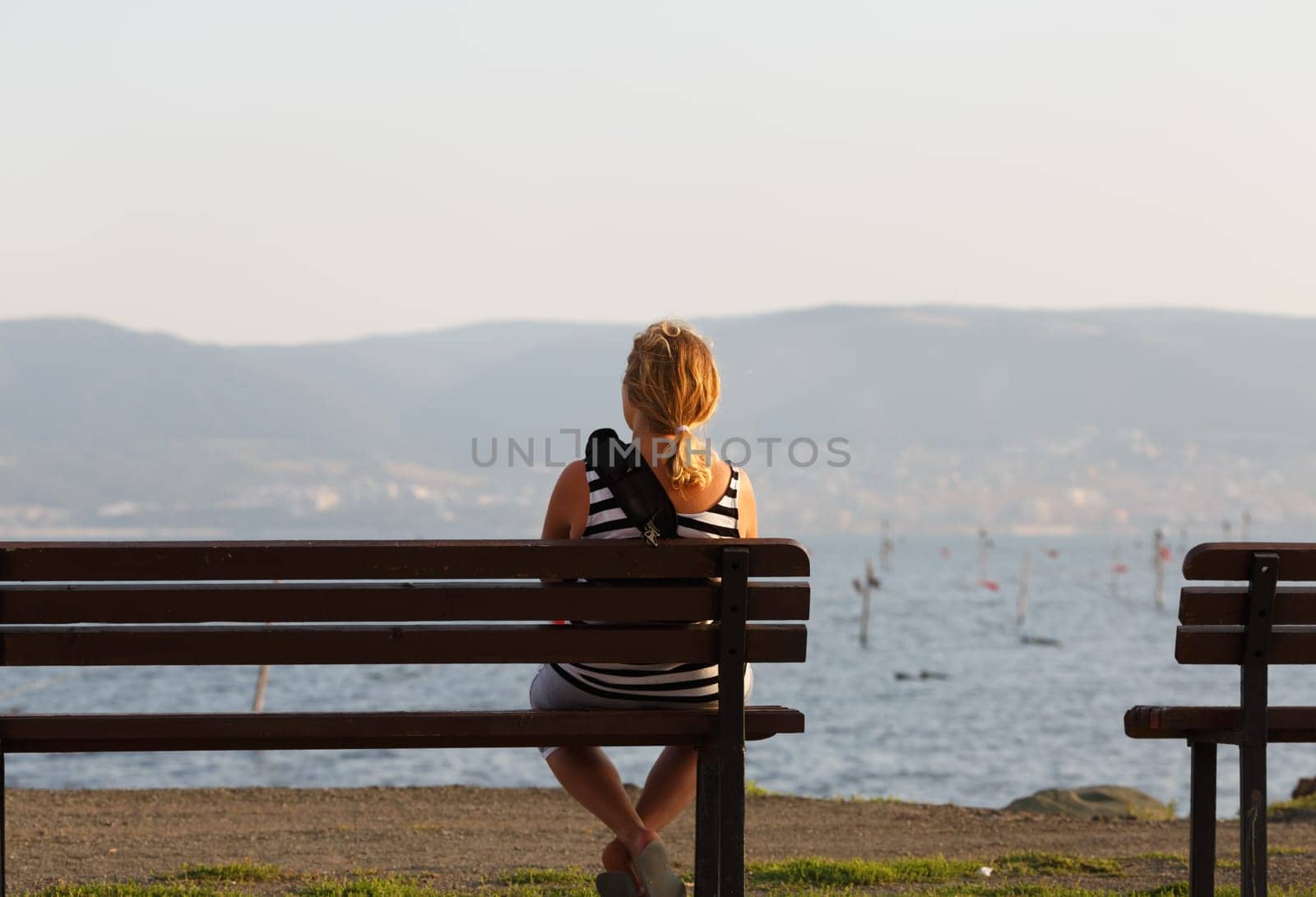 Lonely young woman sitting on a wooden bench and looking at the sea.
