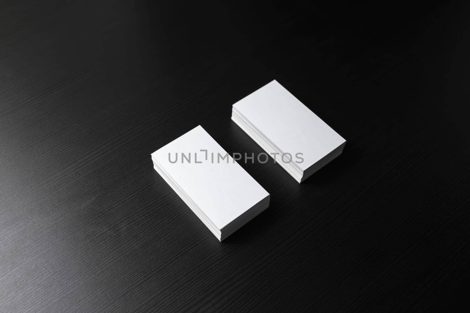 Two blank business cards stacks at black wood table background.