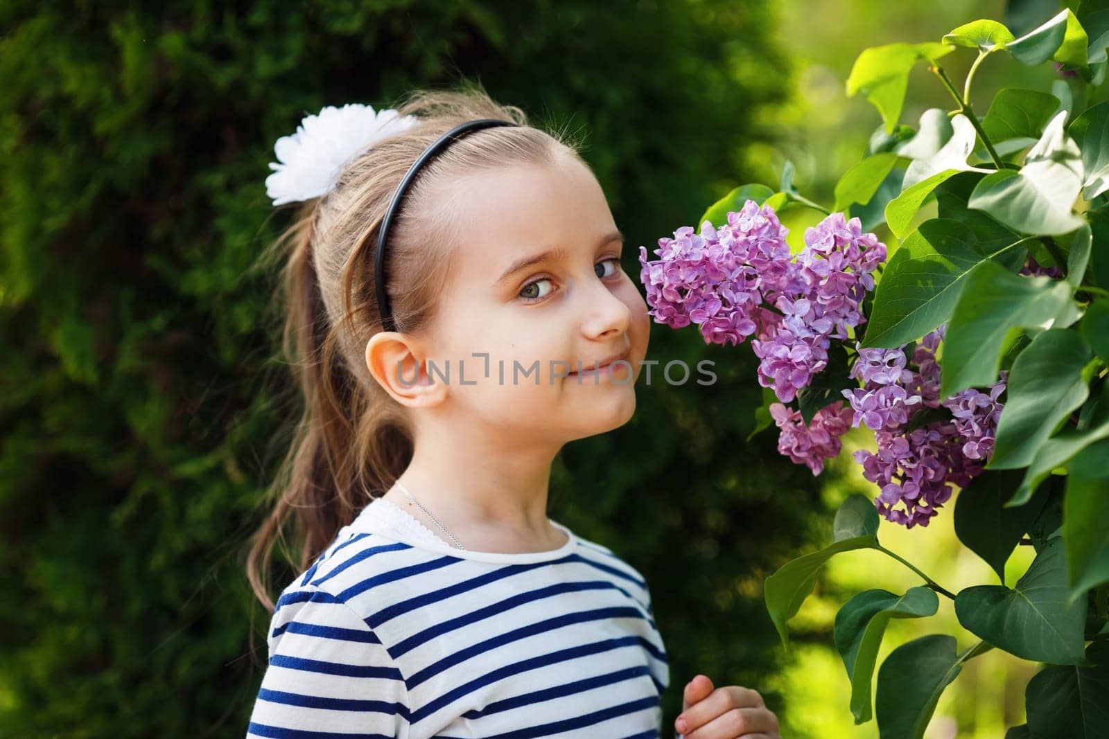 Little girl smelling lilacs in the garden. Beautiful spring day. Selective focus.