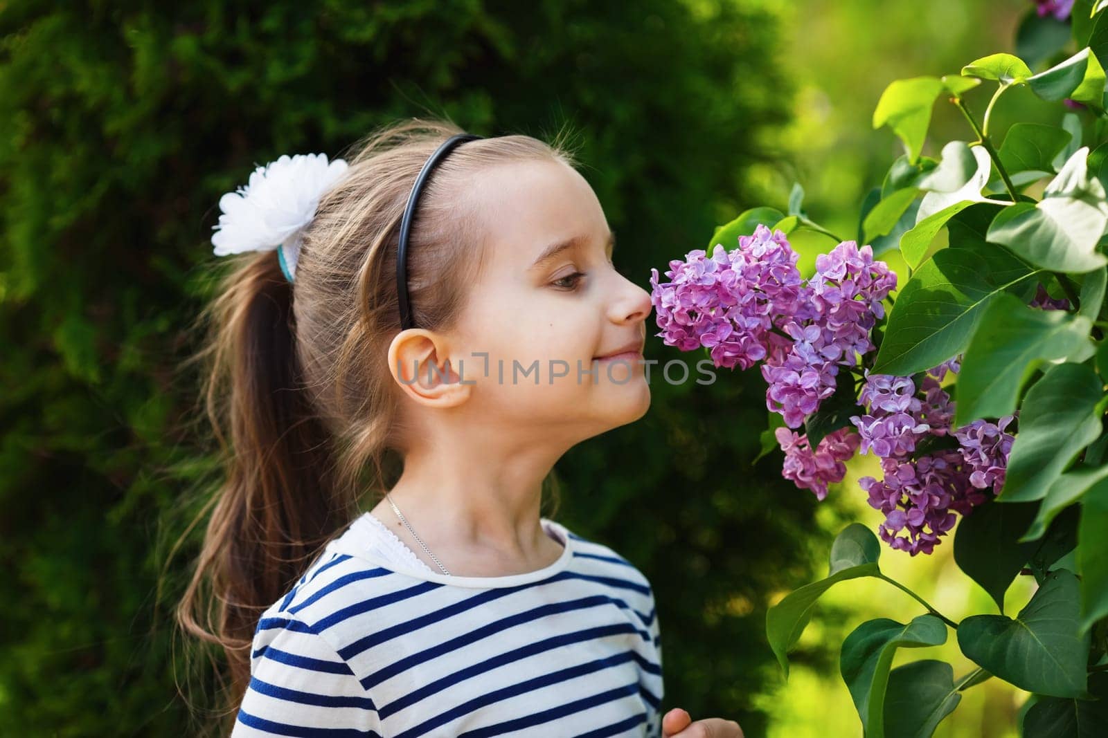 Little girl child smelling lilac flowers in the garden. Selective focus.