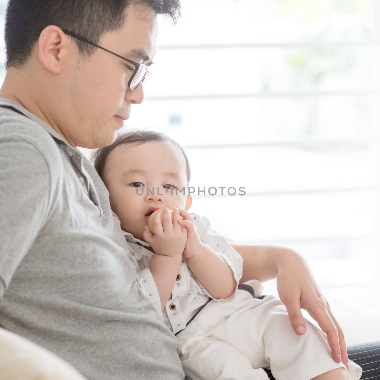 Asian family at home. Father holding baby boy, living lifestyle indoors.