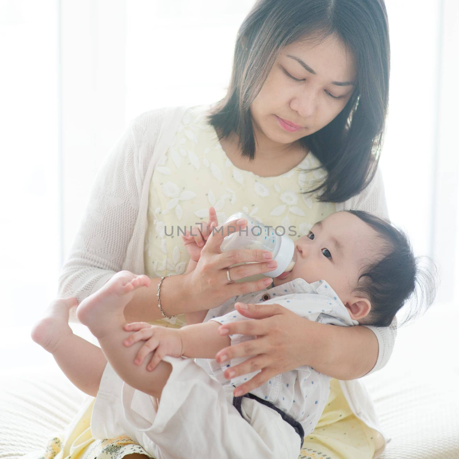 Mother bottle feed formula milk to 9 months old baby boy. Asian family at home, living lifestyle indoors.